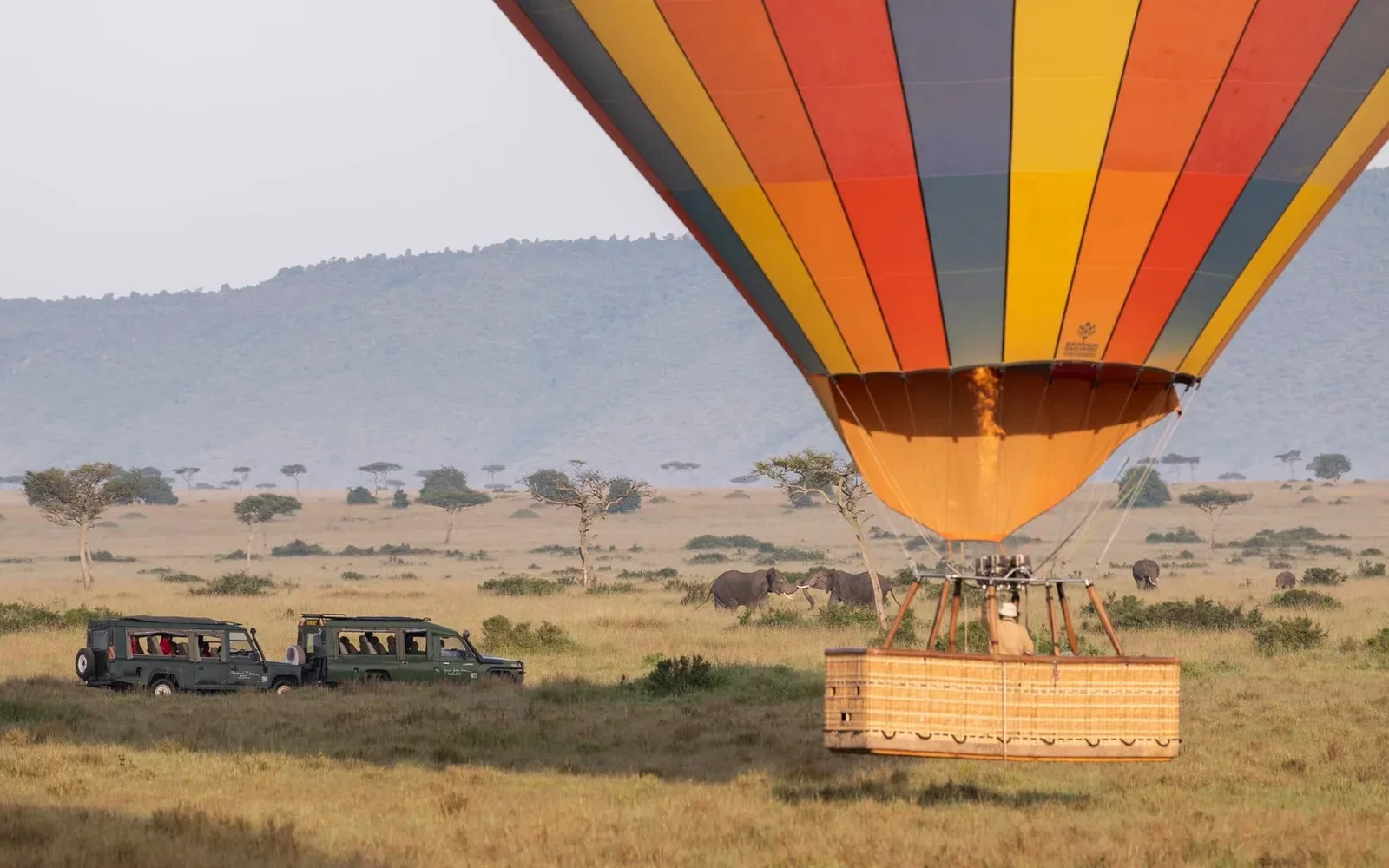 Balloon landing beside safari vehicles with elephants beyond