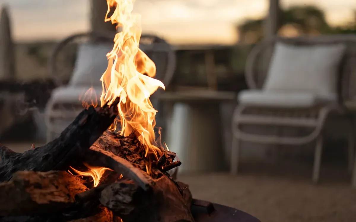 Fire pit burning at dusk beside lodge loungers