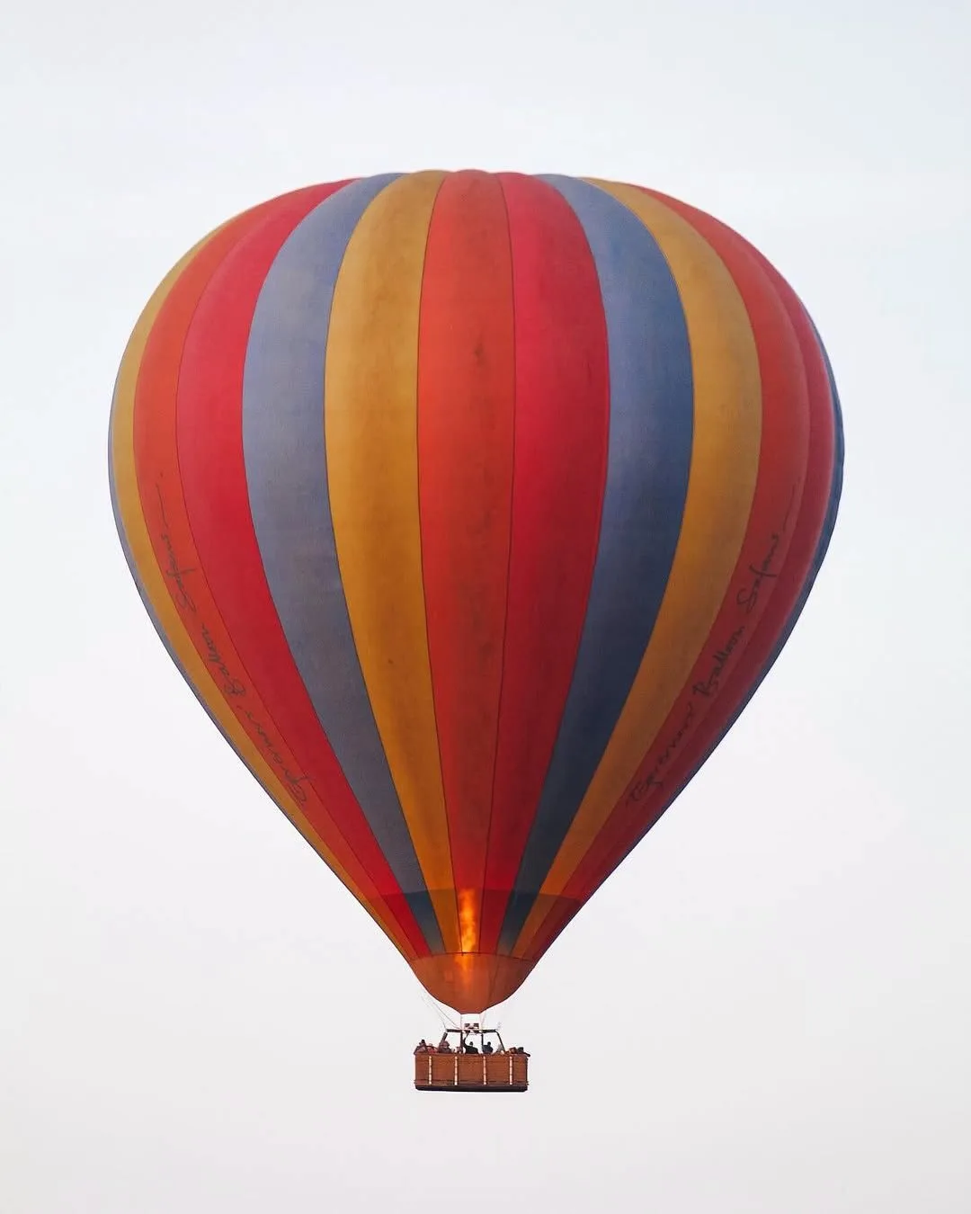 Hot air balloon rising against a pale sky over the Mara