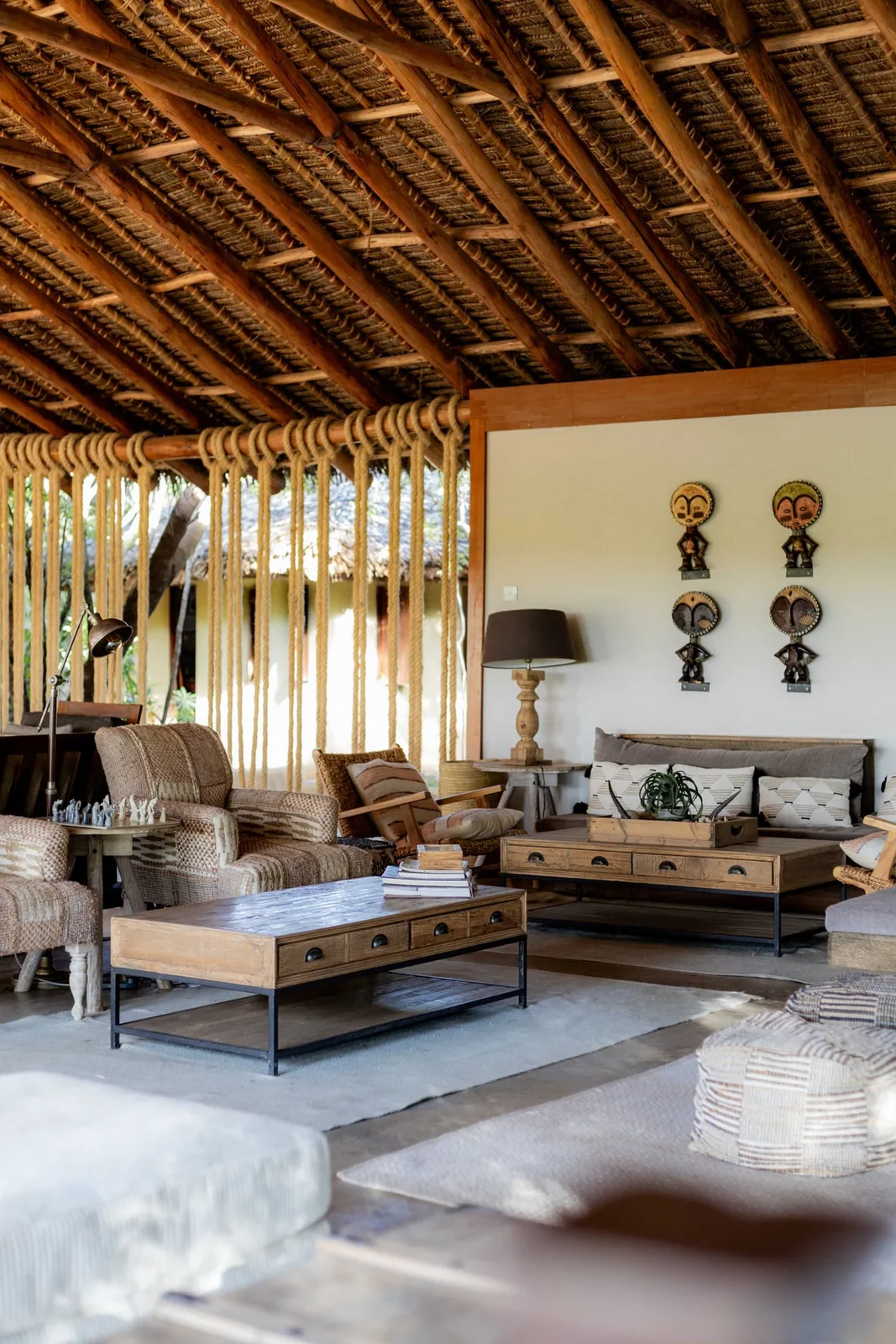 Open sided thatched lodge lounge with woven furniture and carved African masks on the wall