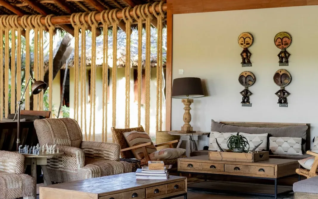 Open sided lodge lounge with a thatched roof, woven chairs and carved African masks