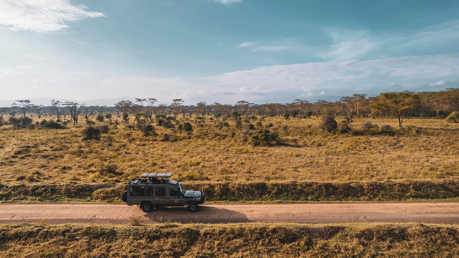 Uthando safari vehicle driving a red dirt road through golden grassland and acacia woodland, seen from above